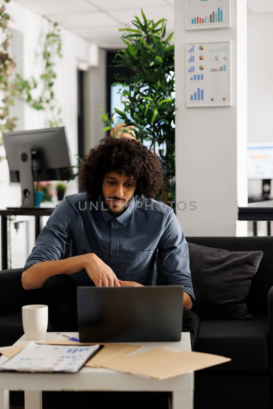 Arab executive manager working at start up project development in business office. Young businessman sitting on couch at workspace and checking marketing research on laptop