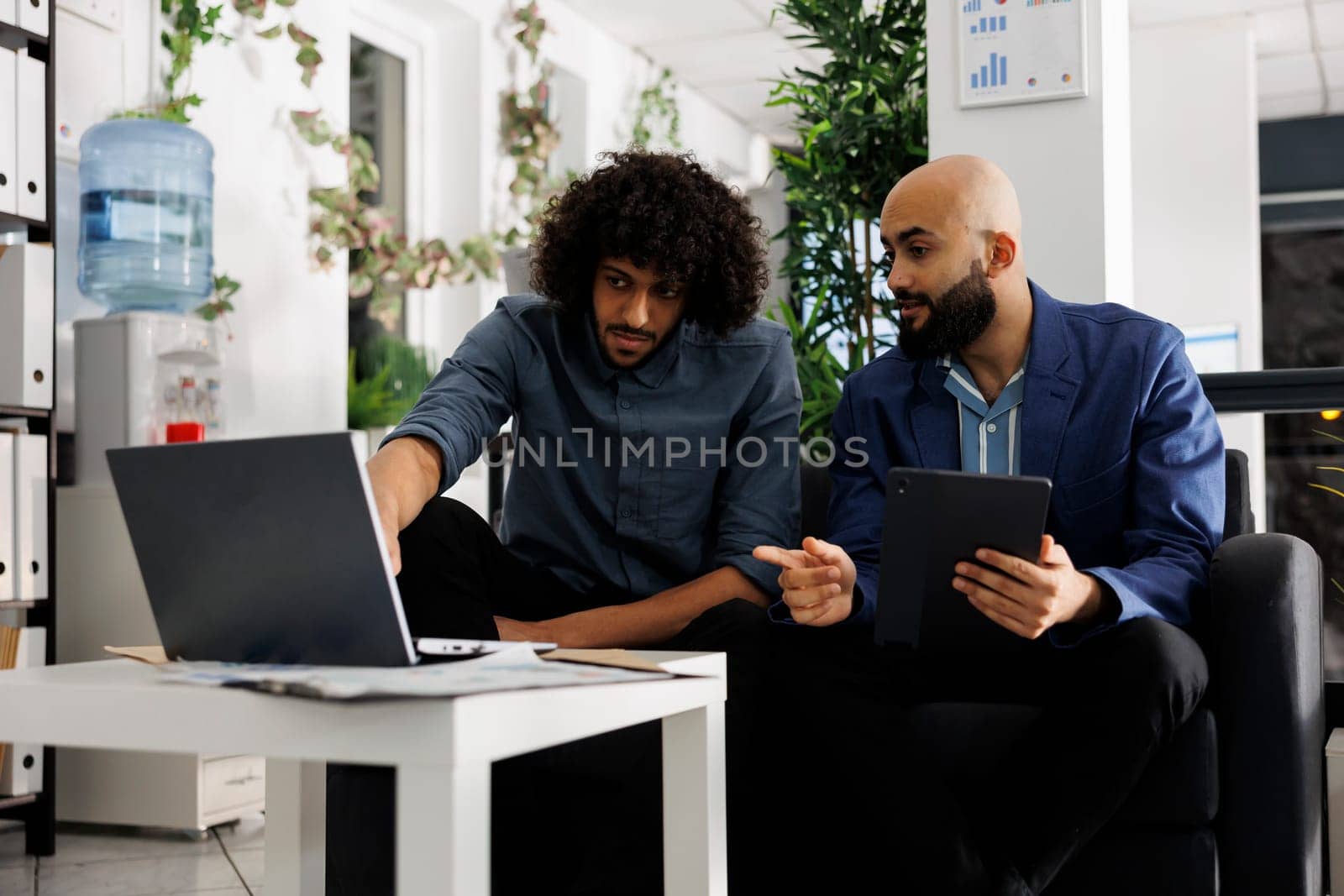 Entrepreneur and colleague discussing project while analyzing data on laptop in business office. Arab employees planning product promotion strategy together in coworking space