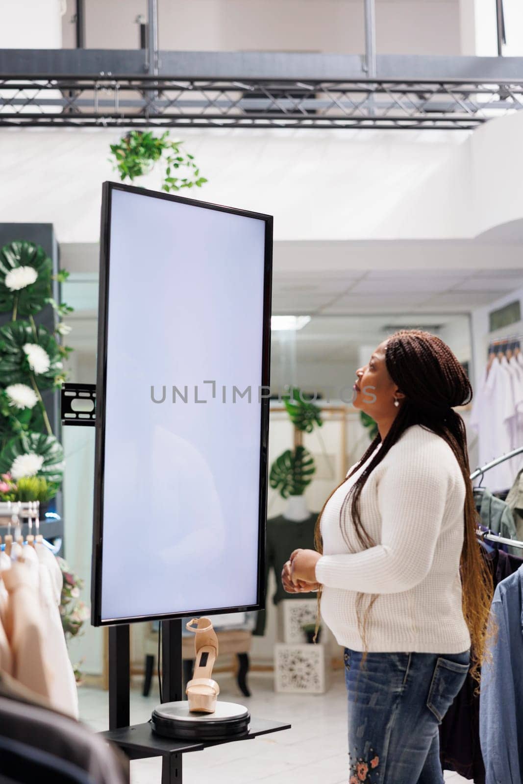 Boutique customer reading information on interactive display board showcasing stiletto shoes for sale. Woman checking advertisement on digital whiteboard promoting brand new collection