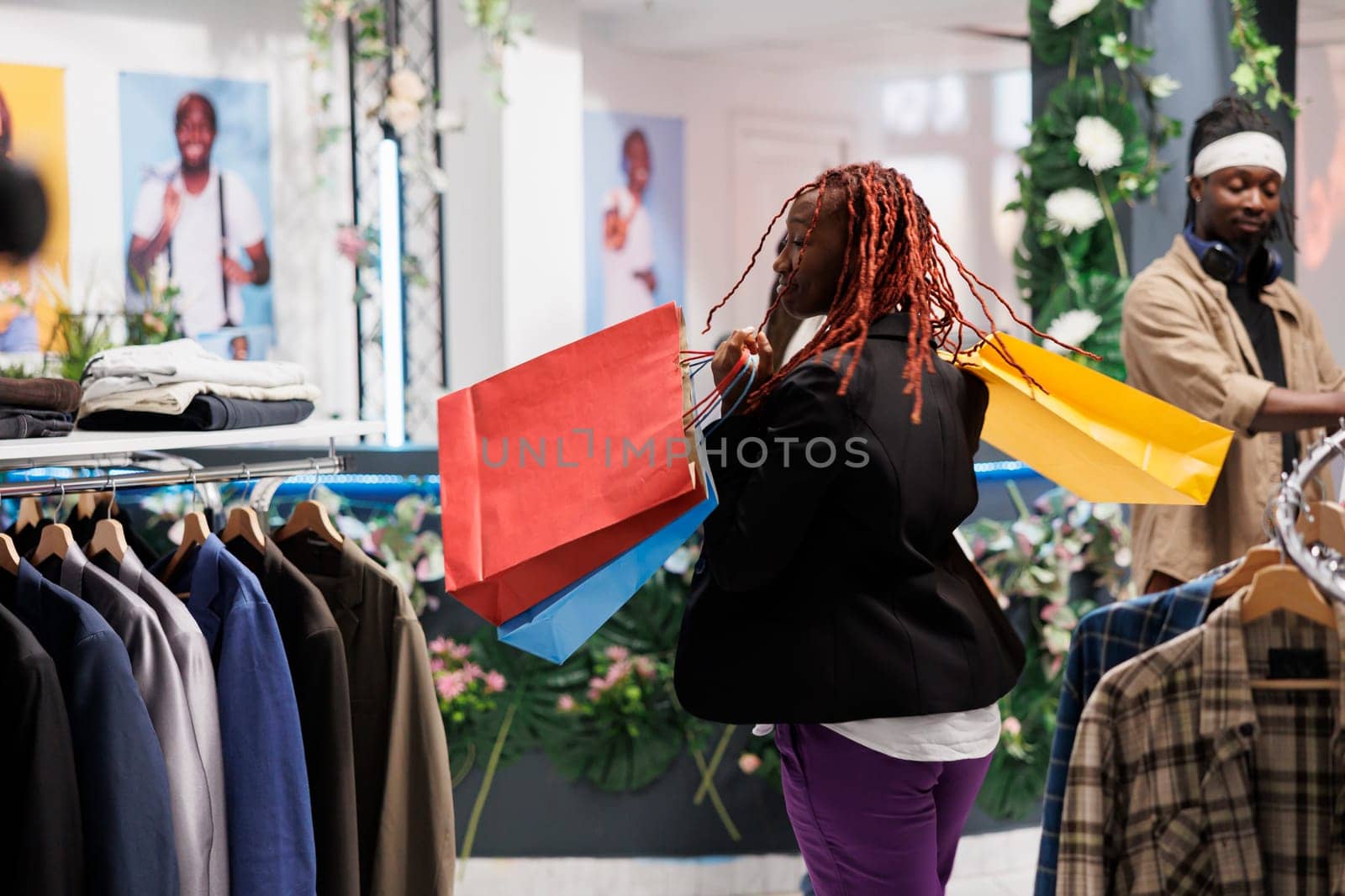 African american woman dancing with joy while holding shopping bags in showroom. Happy young shopper carrying multiple paper packages filled with discounted purchases in clothing store