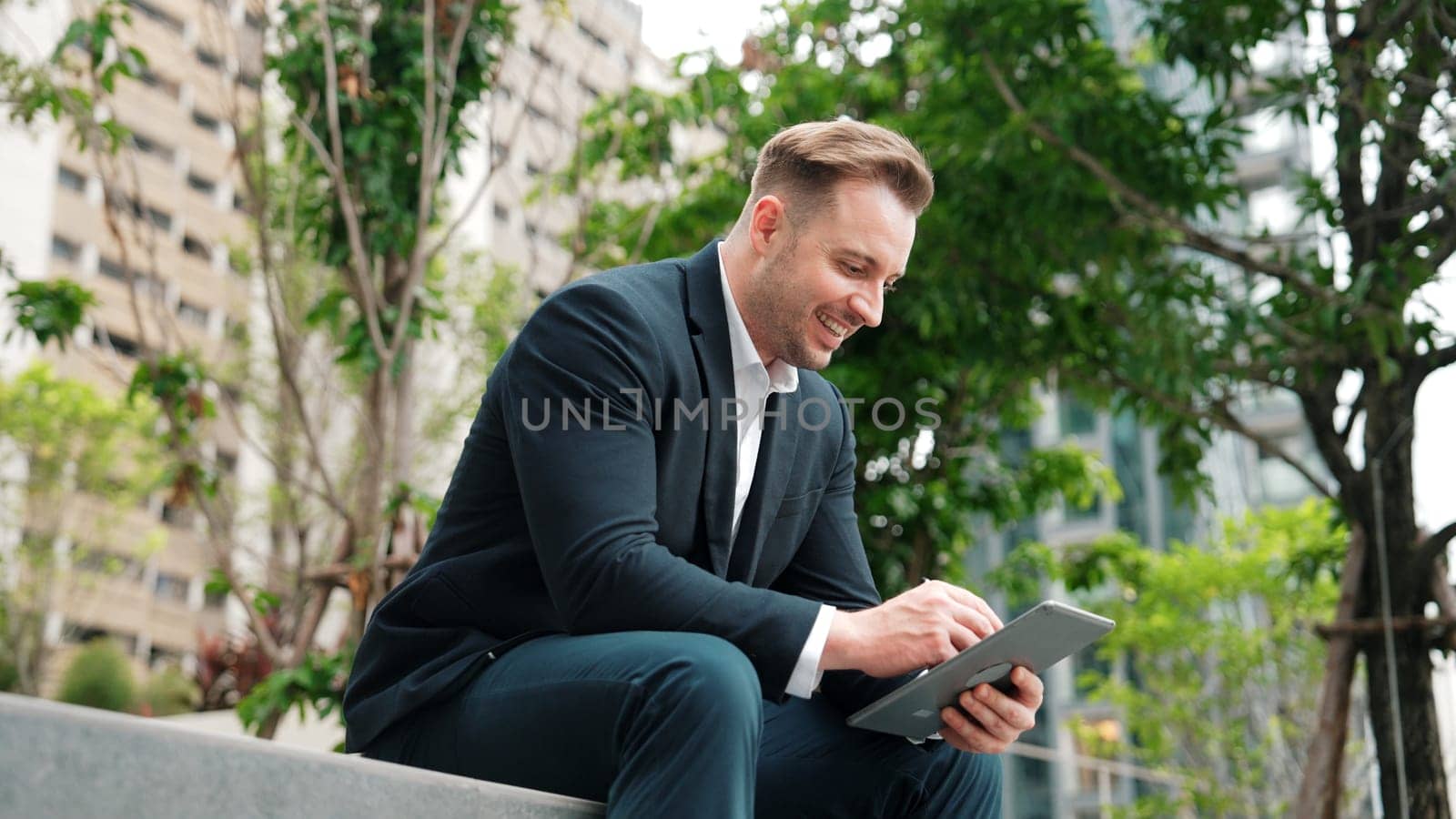 Businessman sitting at park while working on tablet by reading report. Urbane by biancoblue