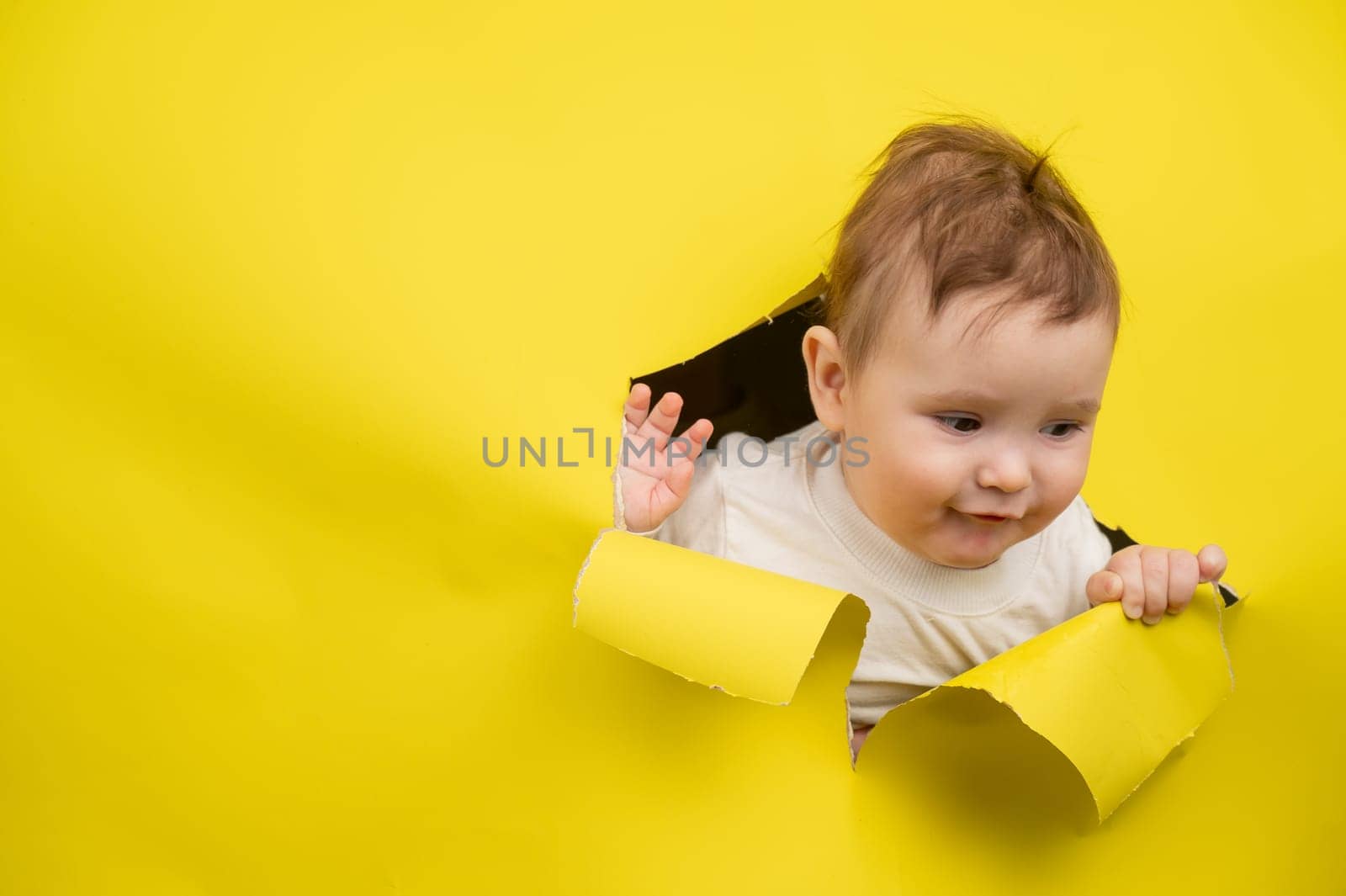 Cute Caucasian baby sticking out of a hole in a paper yellow background