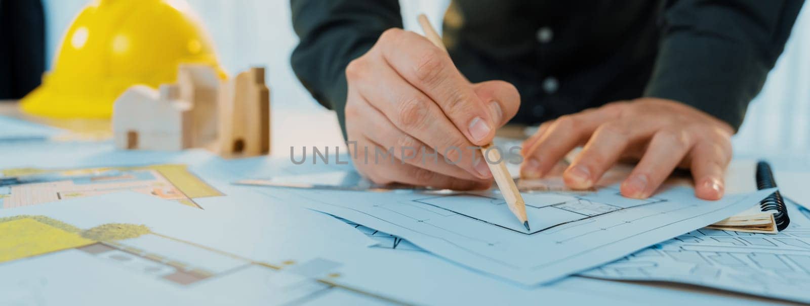 Professional engineer measuring the blueprint. Professional engineer working architectural project at studio on a table with yellow helmet and architectural equipment scatter around. Delineation.