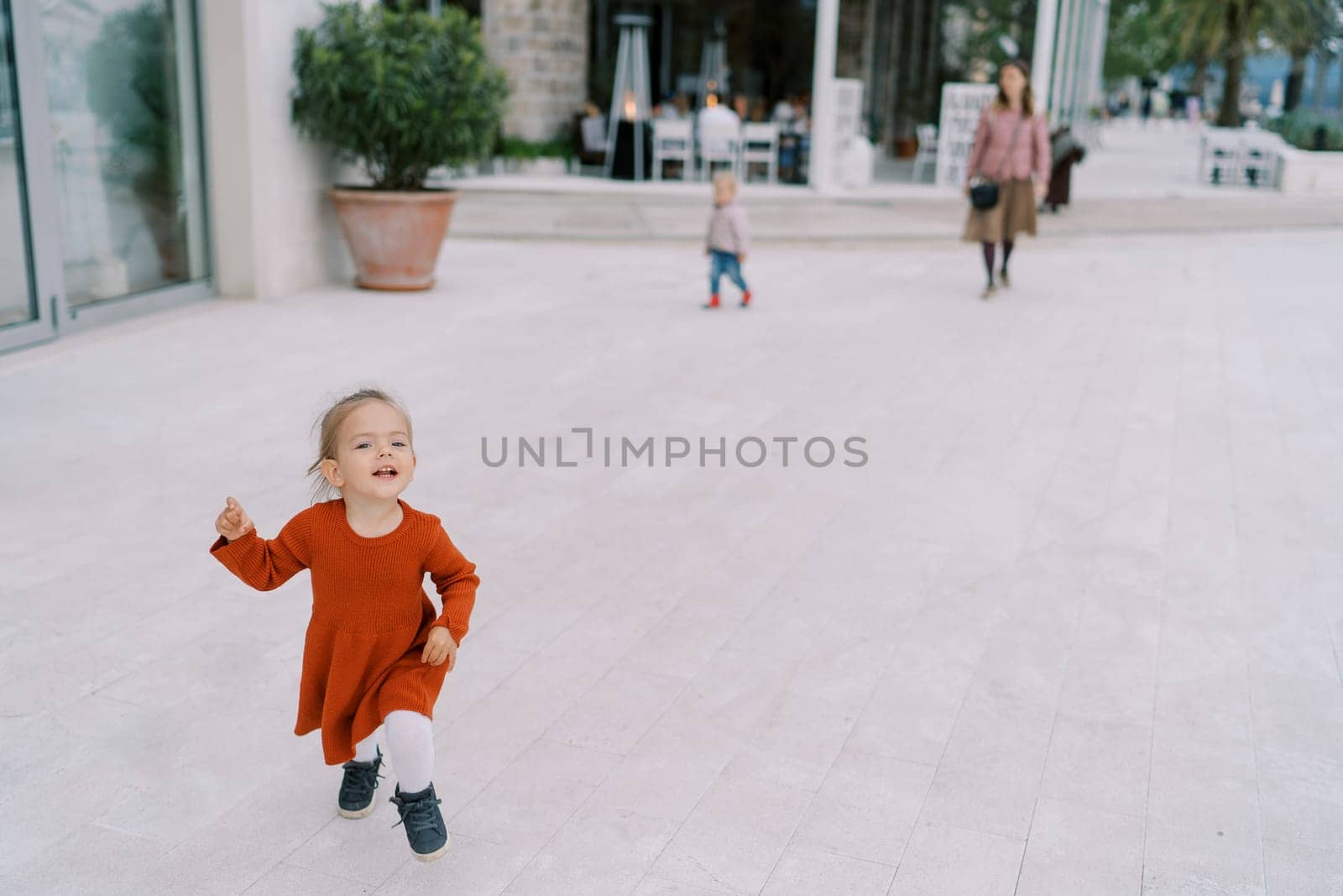 Little girl runs along a wide street, holding her hem. High quality photo