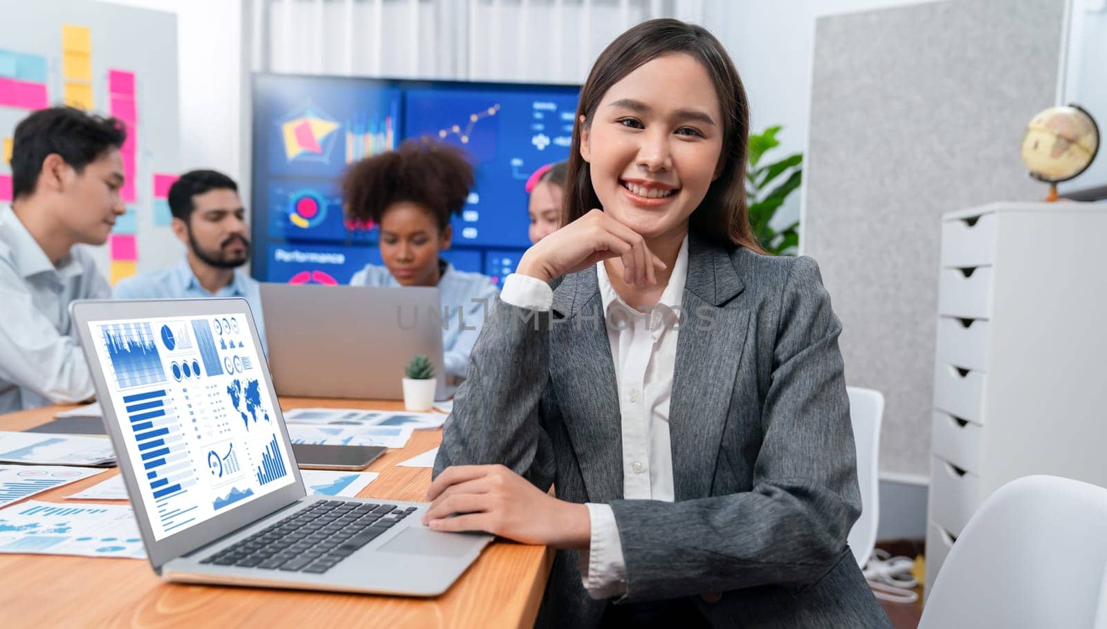 Portrait of happy young asian businesswoman with group of office worker on meeting with screen display business dashboard in background. Confident office lady at team meeting. Concord