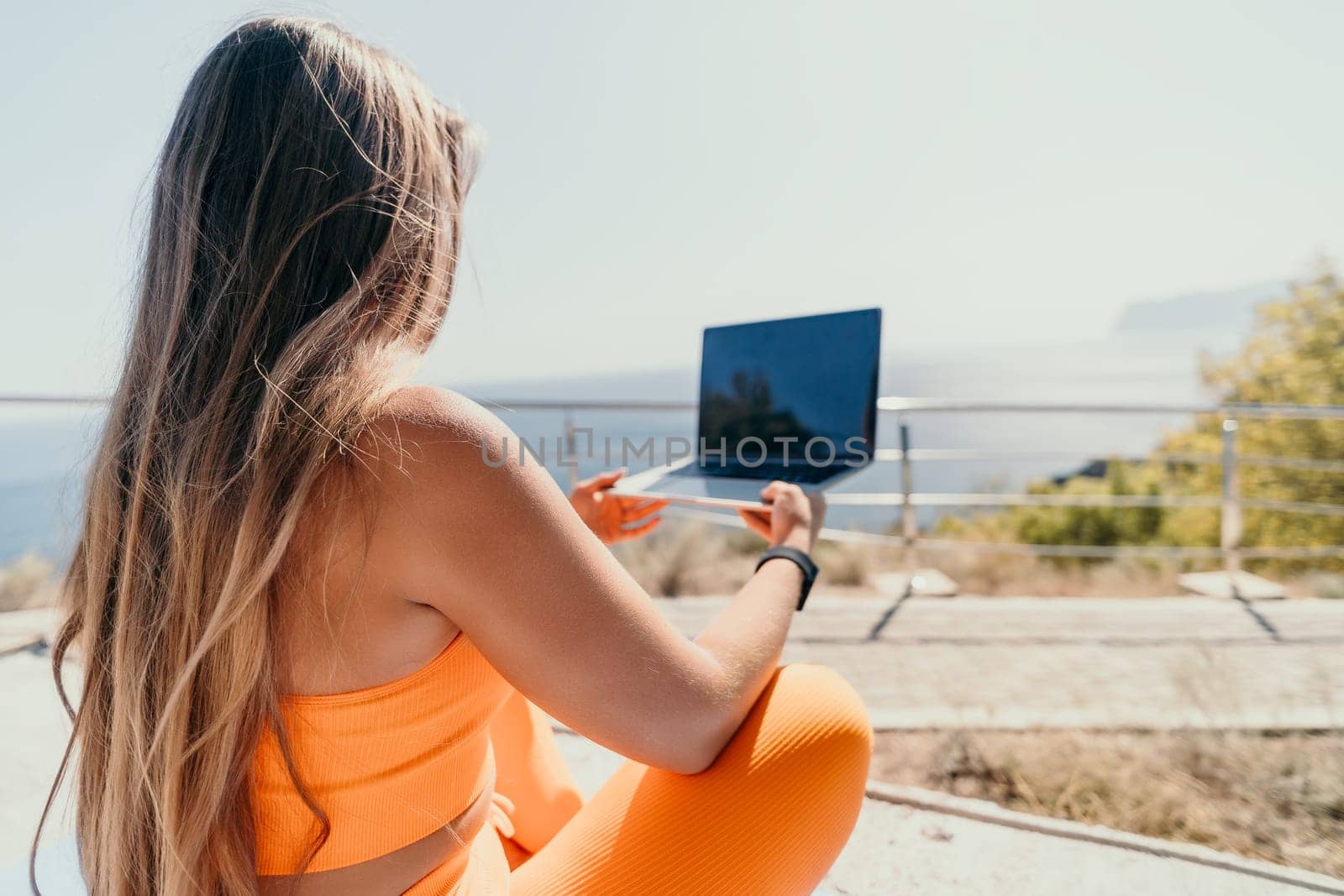 Woman laptop sea. Working remotely on seashore. Happy successful woman female freelancer working on laptop by the sea at sunset, makes a business transaction online. Freelance, remote work on vacation by panophotograph