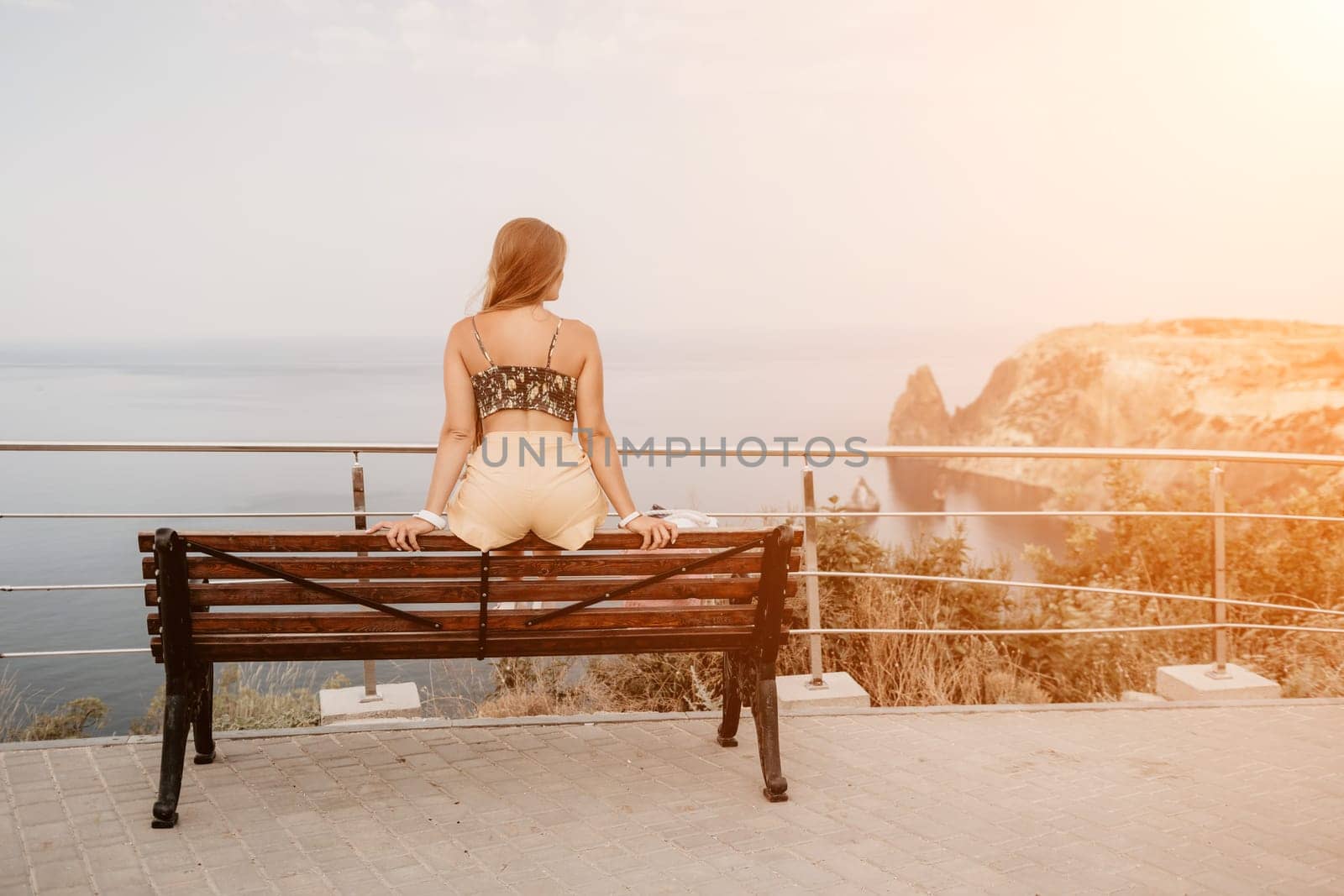 Woman travel sea. Happy tourist taking picture outdoors for memories. Woman traveler looks at the edge of the cliff on the sea bay of mountains, sharing travel adventure journey.