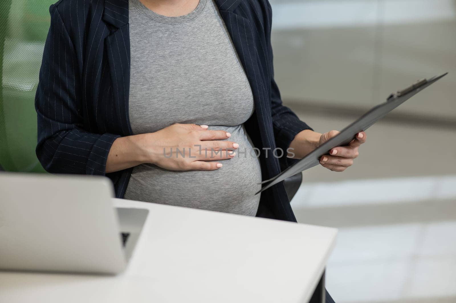 Pregnant woman reading documents on a paper tablet in the office. Close-up of the tummy