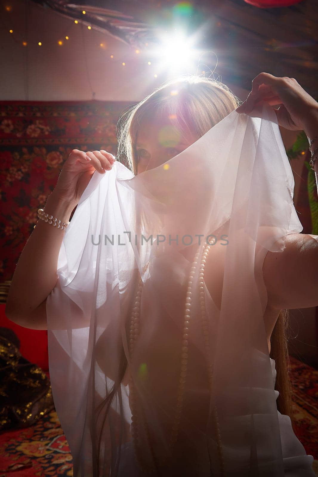 Beautiful European girl looking like Arab woman in red room with rich fabrics and carpets in sultan harem. Photo shoot of an oriental style odalisque. A model poses in sari as indian woman in india