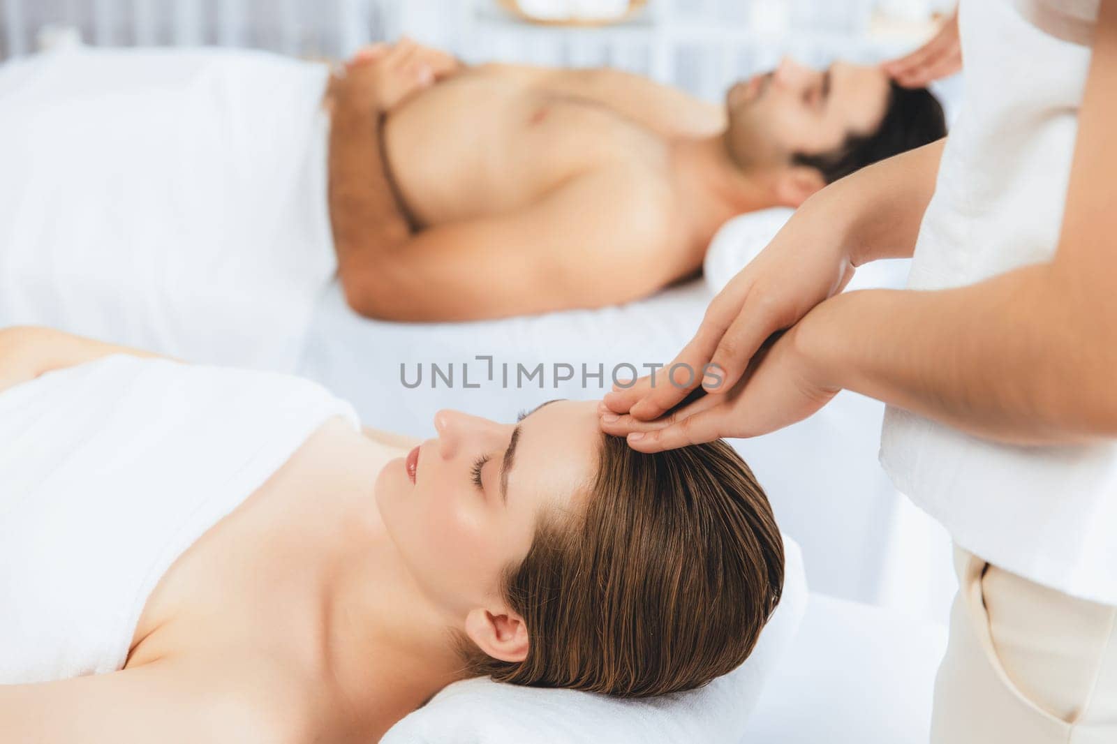 Caucasian couple enjoying relaxing anti-stress head massage and pampering facial beauty skin recreation leisure in dayspa modern light ambient at luxury resort or hotel spa salon. Quiescent