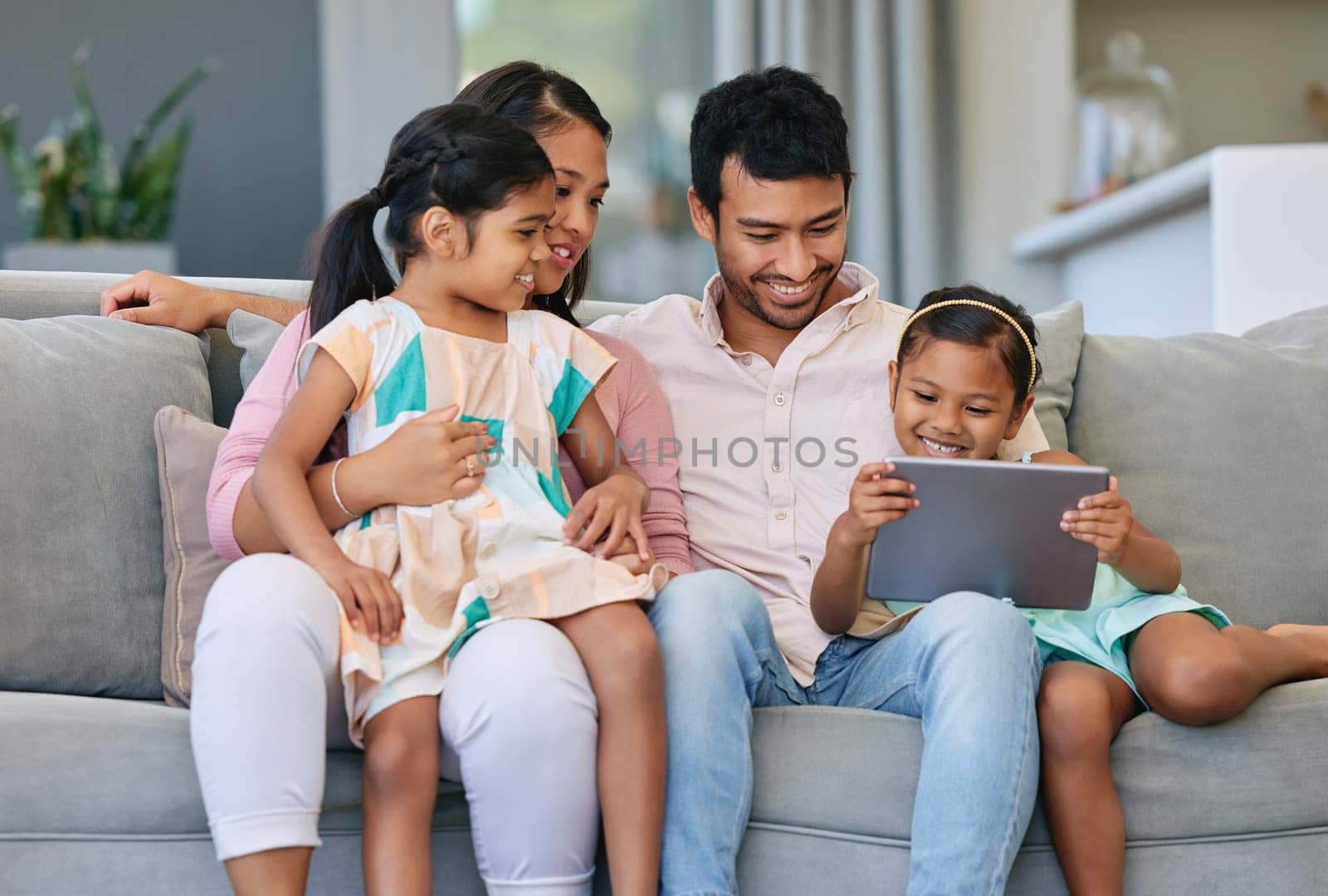 Technology, parents and kids on sofa with tablet, internet and relax together in living room. Mom, dad and girl children on couch with digital app for streaming, games and online connectivity in home by YuriArcurs