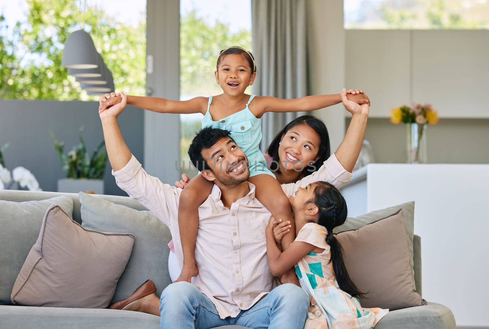 Portrait, parents and kids on sofa with airplane game, bonding and relax together in living room on weekend. Mom, dad and girl children on couch with fun, support and playing in home in Indonesia