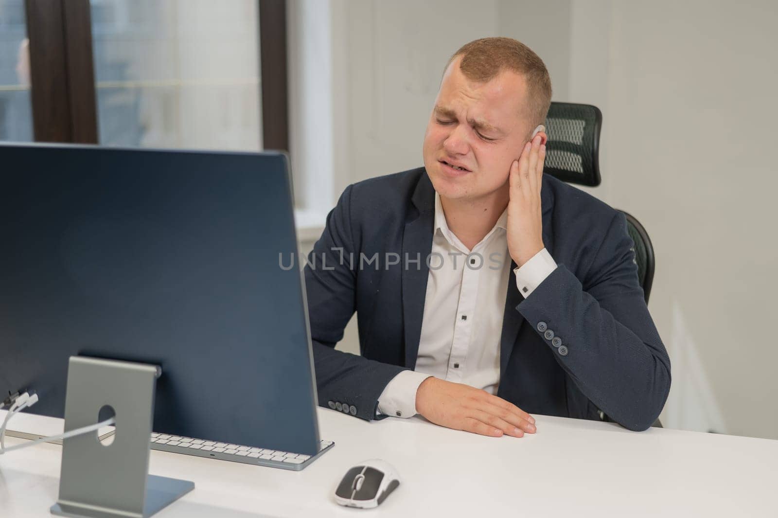 A deaf man works at a computer in the office. Broken hearing aid causing pain