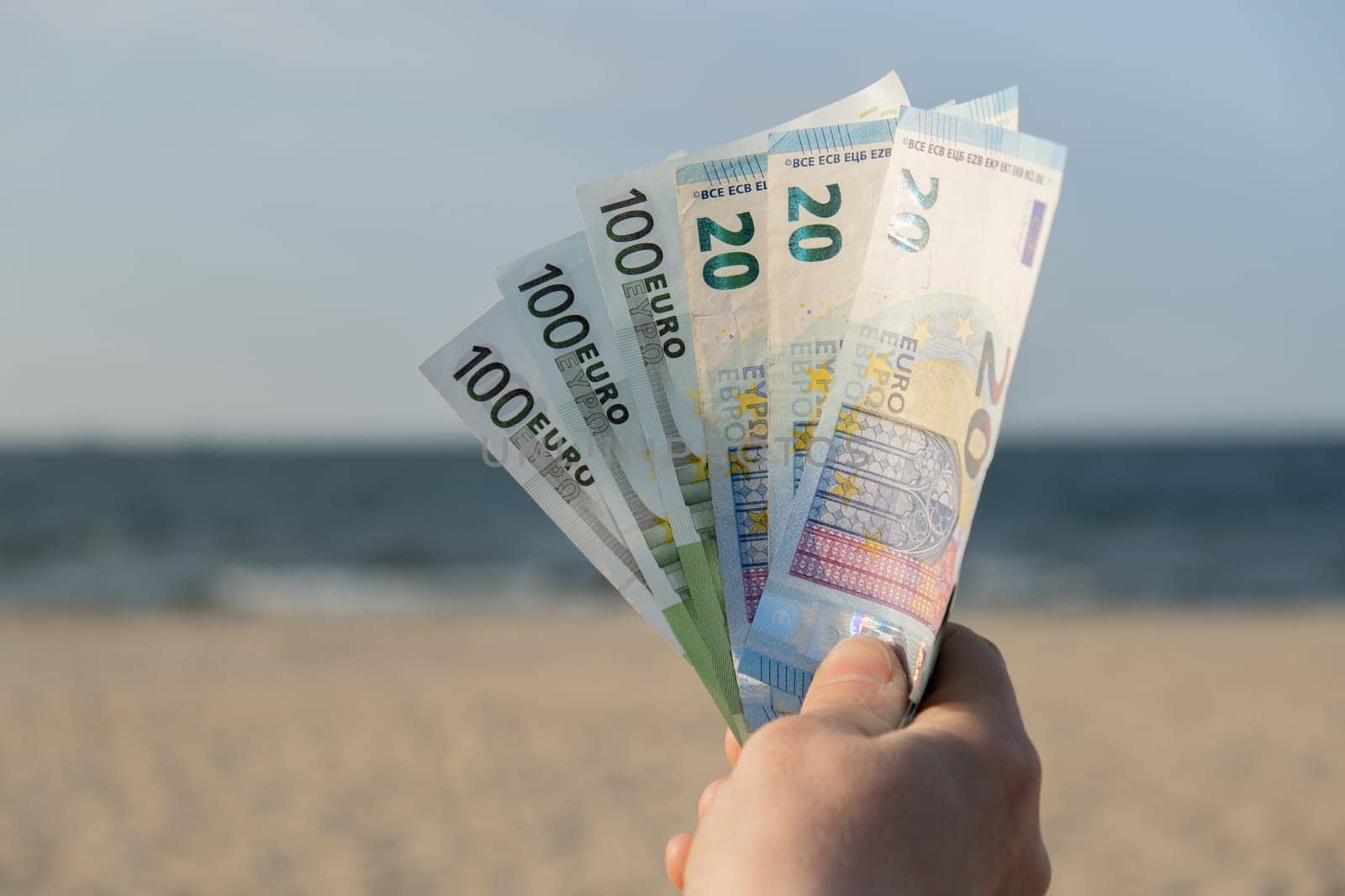 Unrecognizable woman Displaying Spread of Cash euros bills on sandy beach coastline. Concept finance saving money for holiday vacation. Costs in travel holidays. Extra money by anna_stasiia