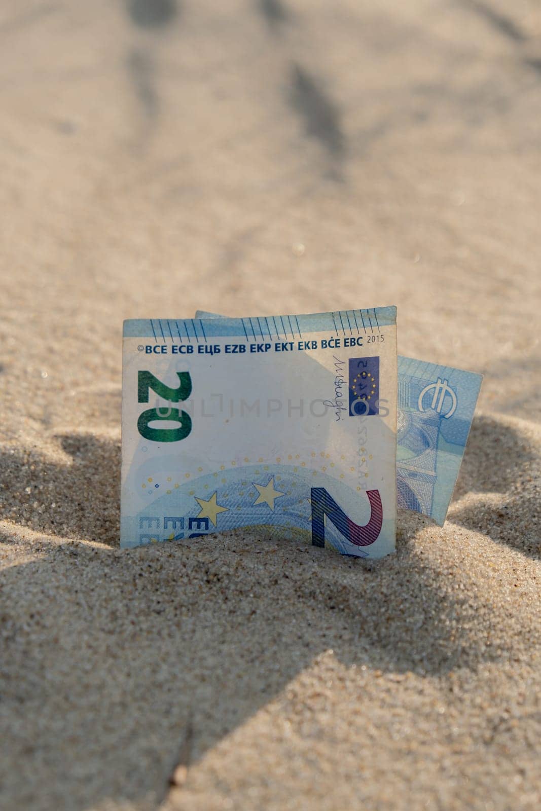 Money 20 euros bills in sandy beach. Concept finance saving money for holiday vacation. Costs in travel holidays by anna_stasiia
