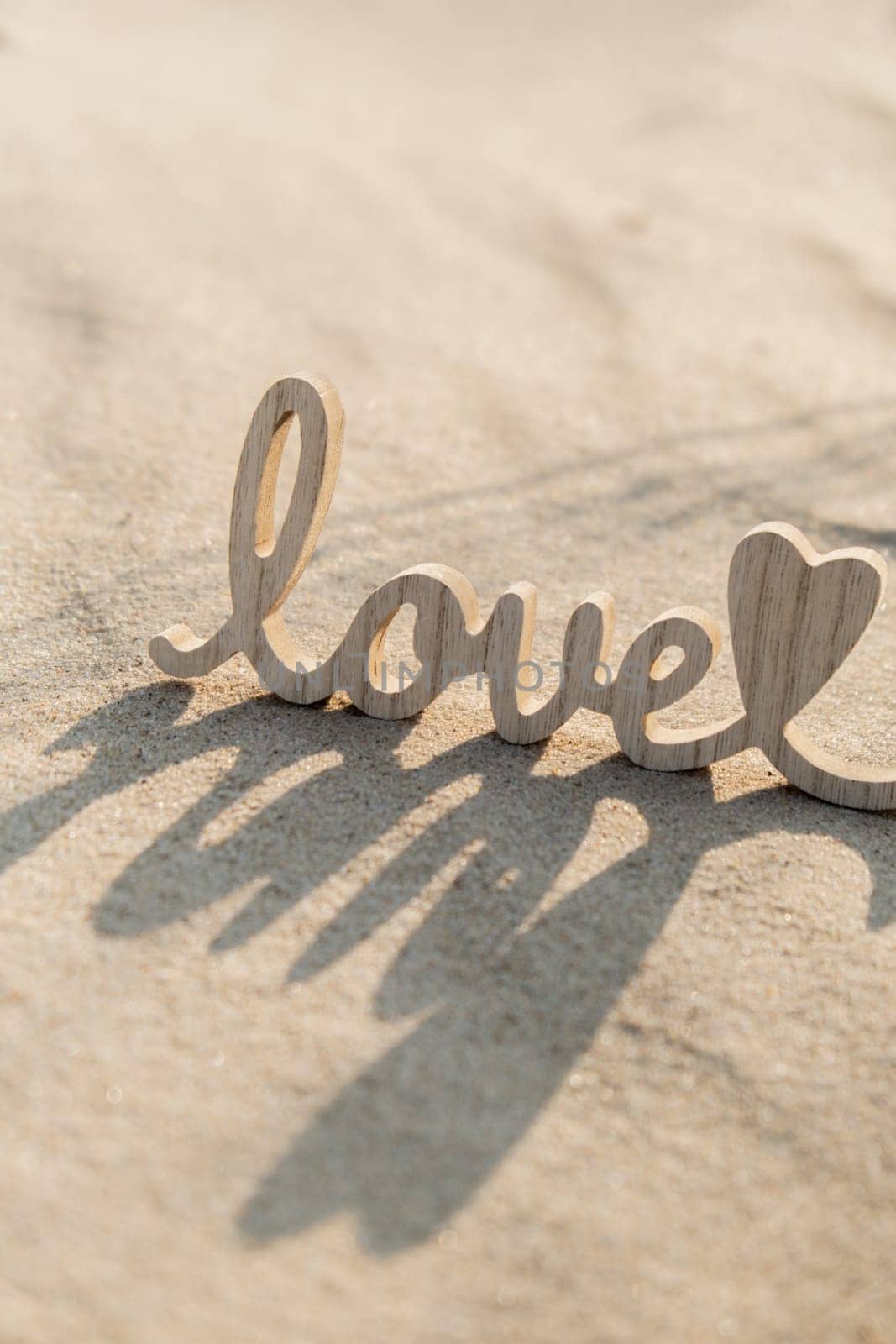 Wooden word love on sandy beach background. Concept of romantic holiday anniversary, proposal, valentines day greeting card, postcard. Letter text in tropical vacation Sand surface. Deep shadows Love is all you need