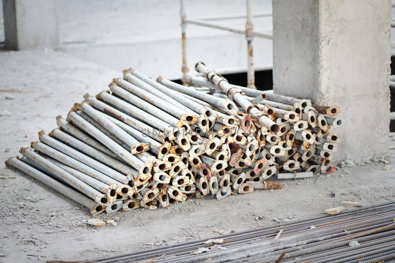 Scaffolding racks in disassembled form lie near a reinforced concrete column on a construction site.