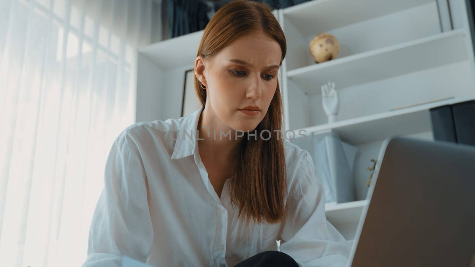 Young businesswoman sitting on the crouch using laptop computer for prim work on internet. Secretary or online content writing working at home. Remote working in domestic lifestyle/