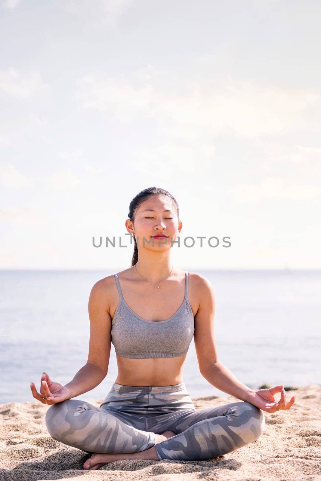 young asian woman doing meditation at beach sitting with legs crossed, concept of mental relaxation and healthy lifestyle, copy space for text