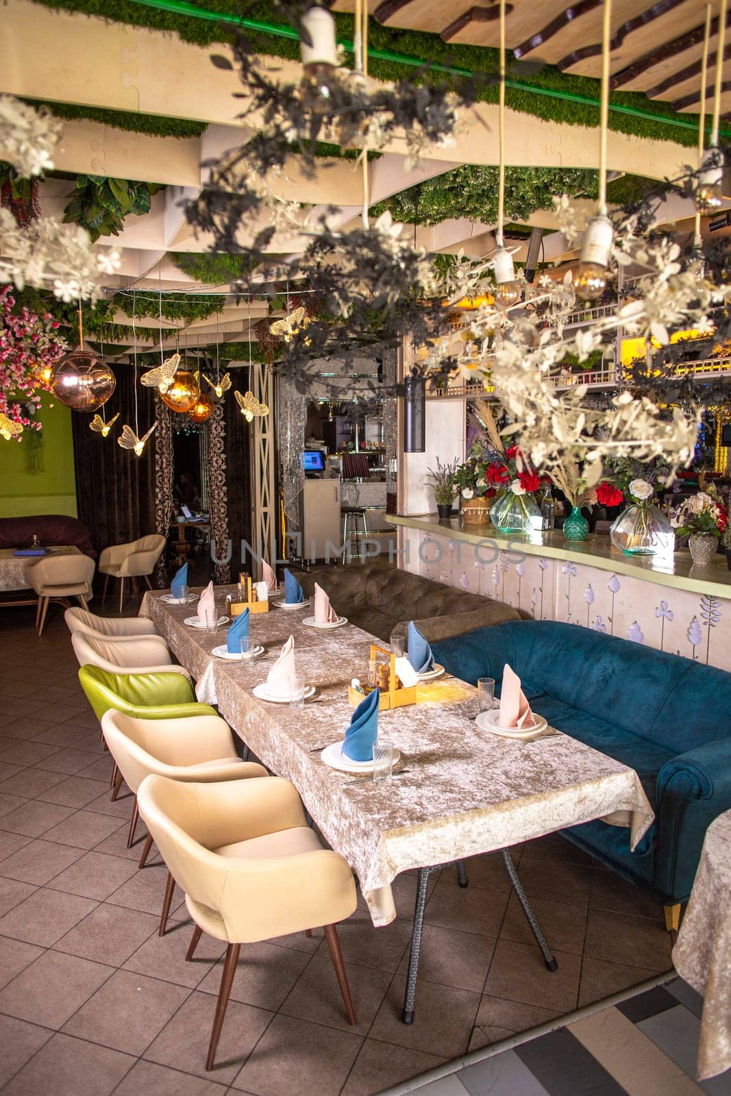 Modern restaurant design with nature touch. Green plants, flowers on walls and ceiling. Long table with glasses, cloth napkins.