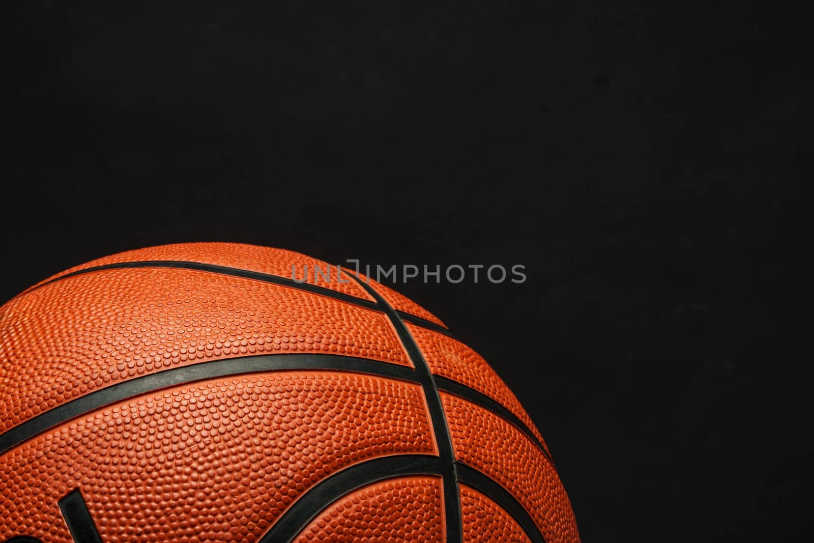 This close-up shot showcases a basketball resting on a black background. The textured surface of the basketball contrasts sharply with the dark backdrop, emphasizing its details.