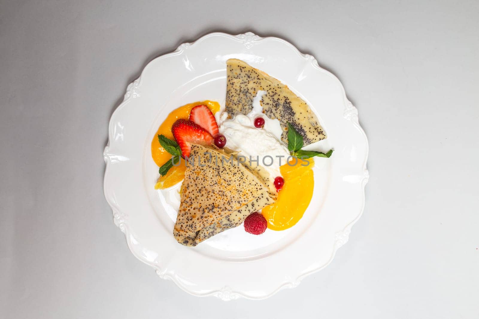 Delicious poppy seed pancakes with berries, orange slices and cream on a white background by Pukhovskiy