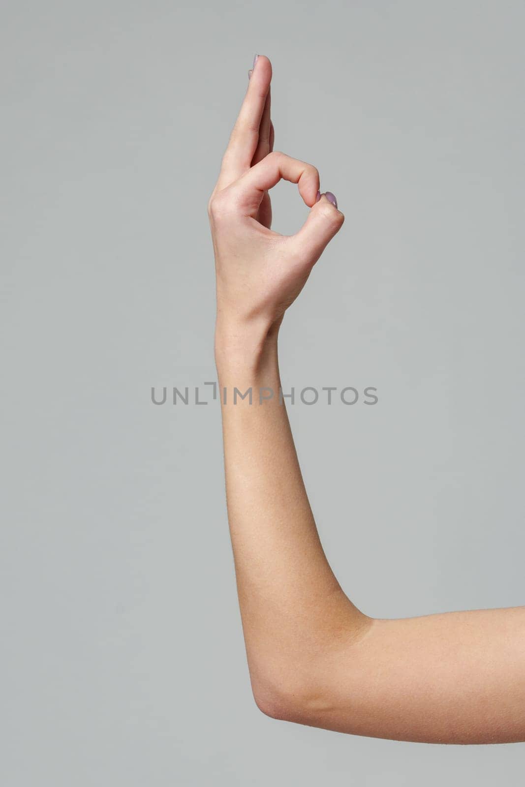 Female hand showing OK sign on gray background by Fabrikasimf