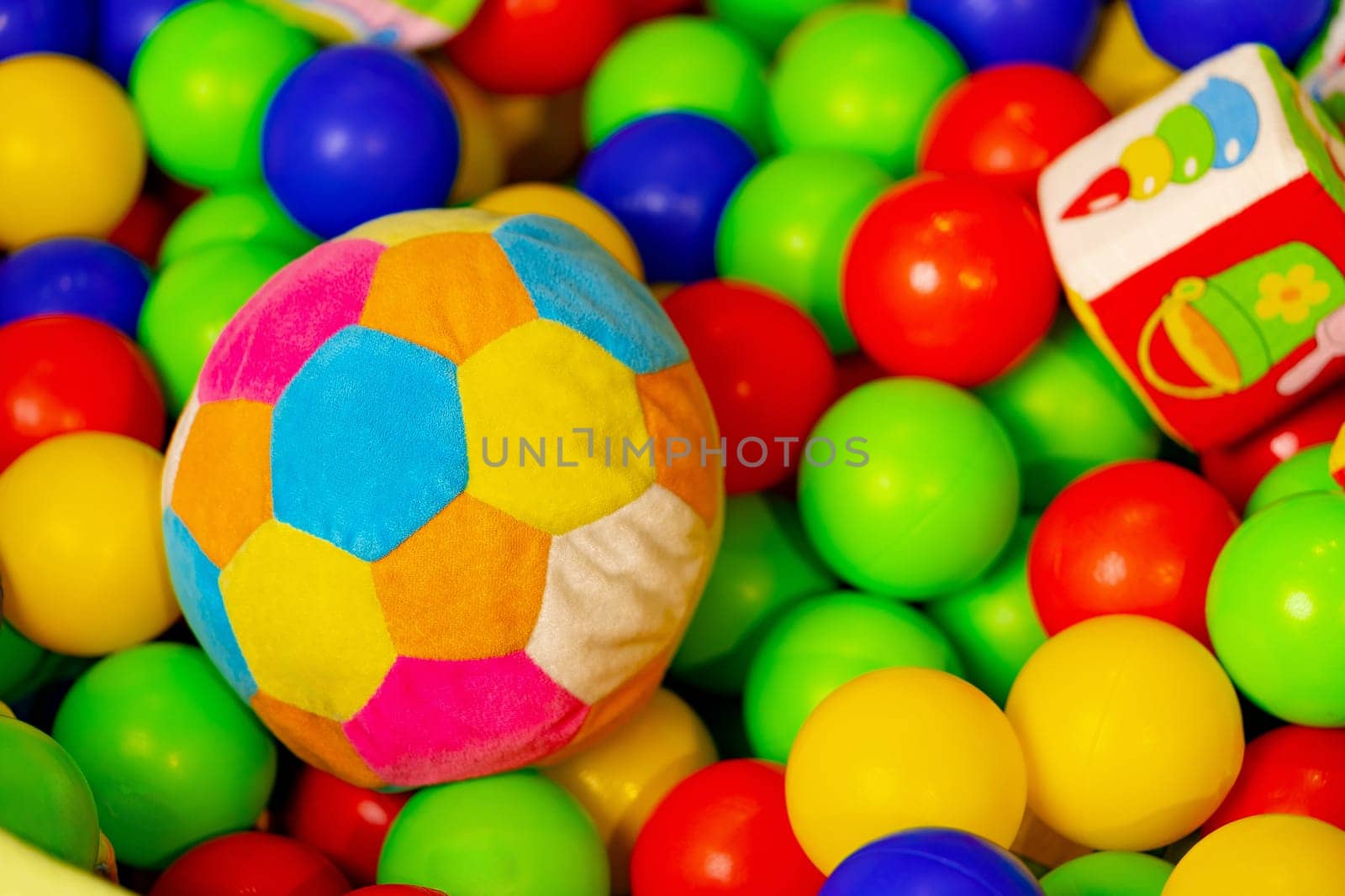 A vibrantly colored soft ball and a small toy truck rest among a multitude of red, yellow, blue, and green plastic balls in a play area, suggesting a lively and fun atmosphere typically found in a childrens indoor playground.
