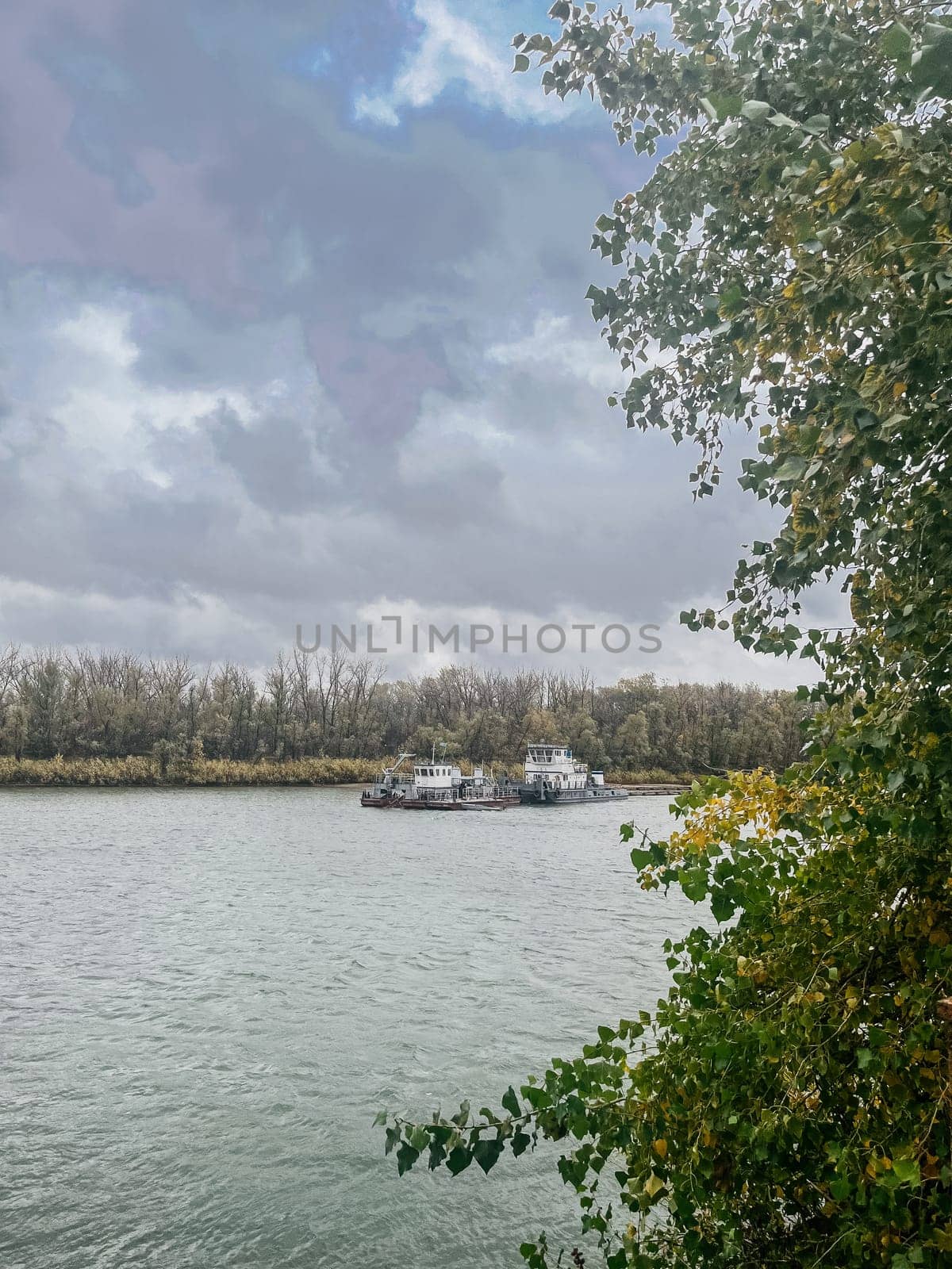 Tugboats on the river with an overcast sky and autumn trees on the shore by Pukhovskiy