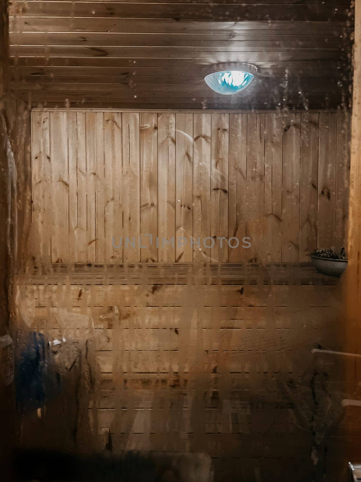 Inside view of a traditional finnish sauna room with wooden walls and benches, and a light on the ceiling.