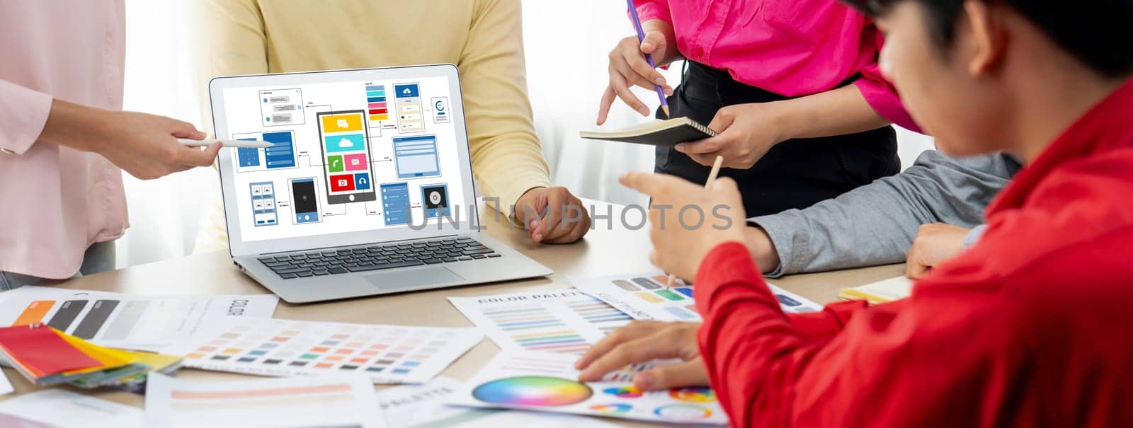 Cropped image of interior designer team presents color by using color swatches while laptop displayed UI and UX designs for mobiles app and website. Creative design and business concept. Variegated.