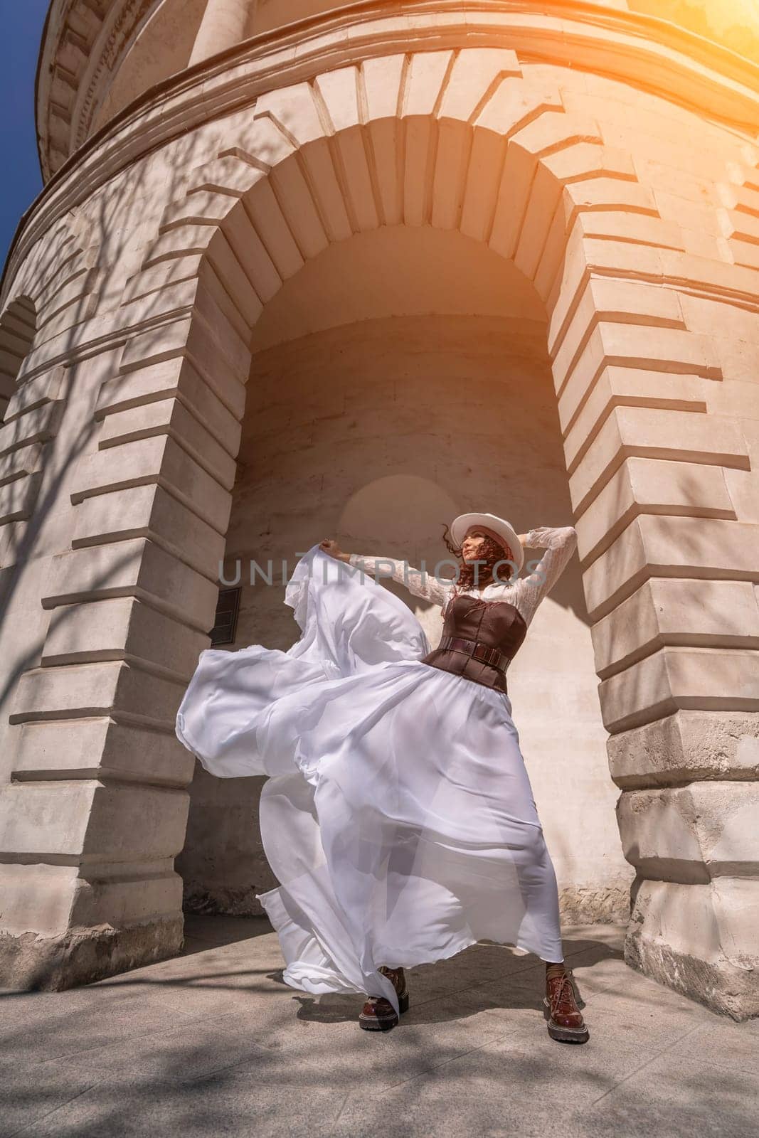Stylish woman building city. A dancer in a long white skirt dances in front of a building with an arch. The skirt develops in the wind