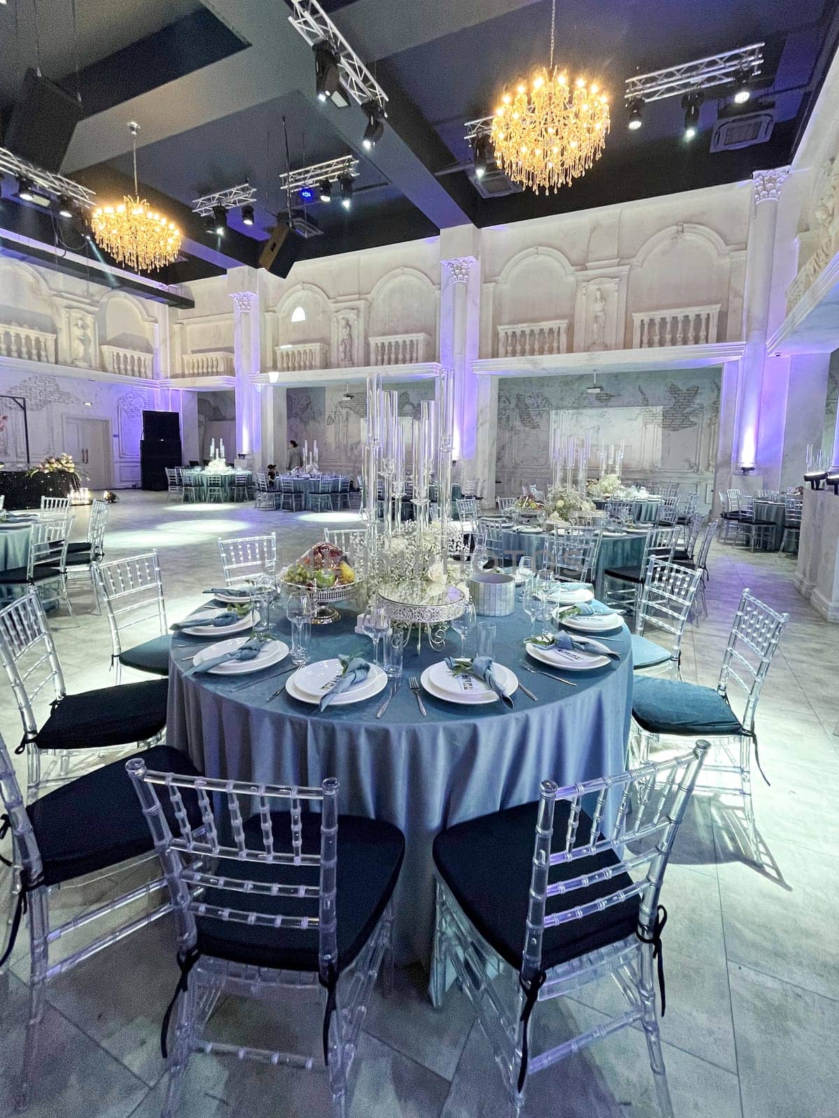 A large, elegant wedding reception hall with round tables, crystal chandeliers, and a balcony overlooking the dance floor.