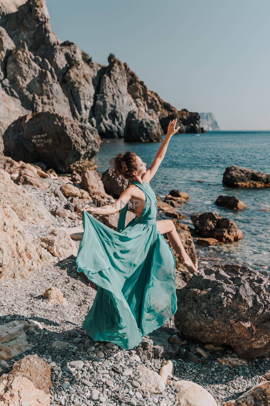 Woman green dress sea. Woman in a long mint dress posing on a beach with rocks on sunny day. Girl on the nature on blue sky background. by Matiunina