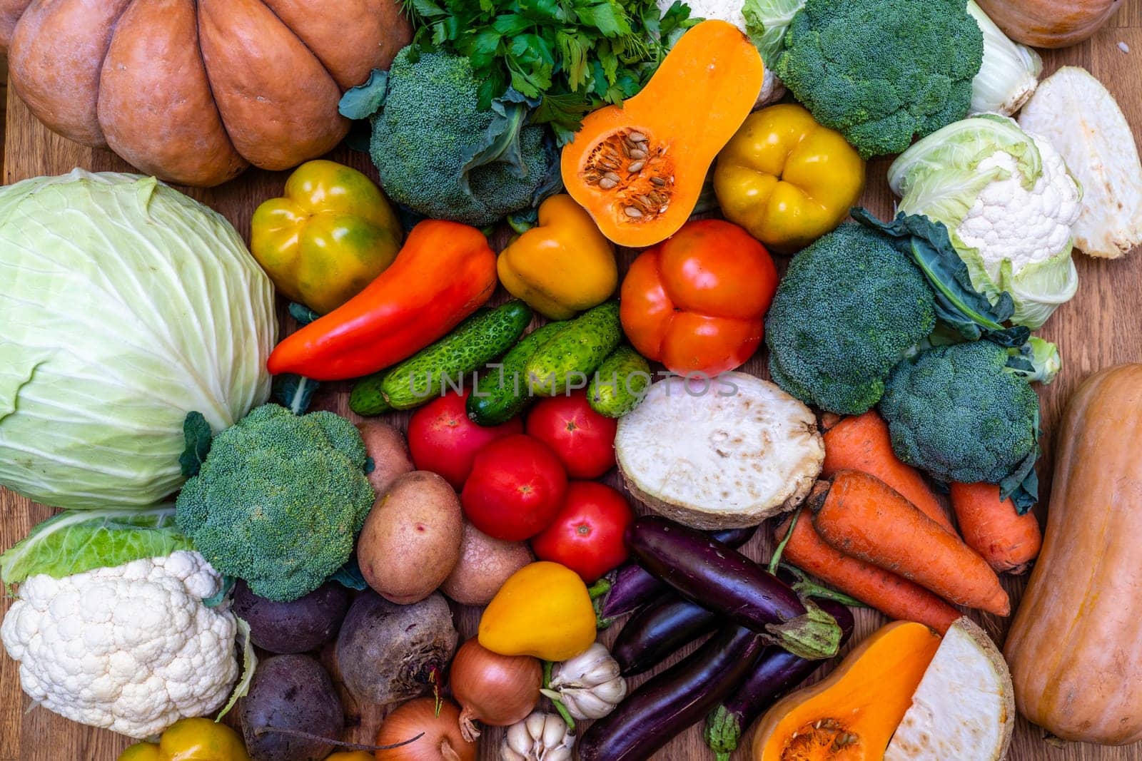 Various vegetables are laid out on a wooden table. Large assortment of vegetables food. pumpkin cabbage broccoli pepper tomatoes carrots and others.