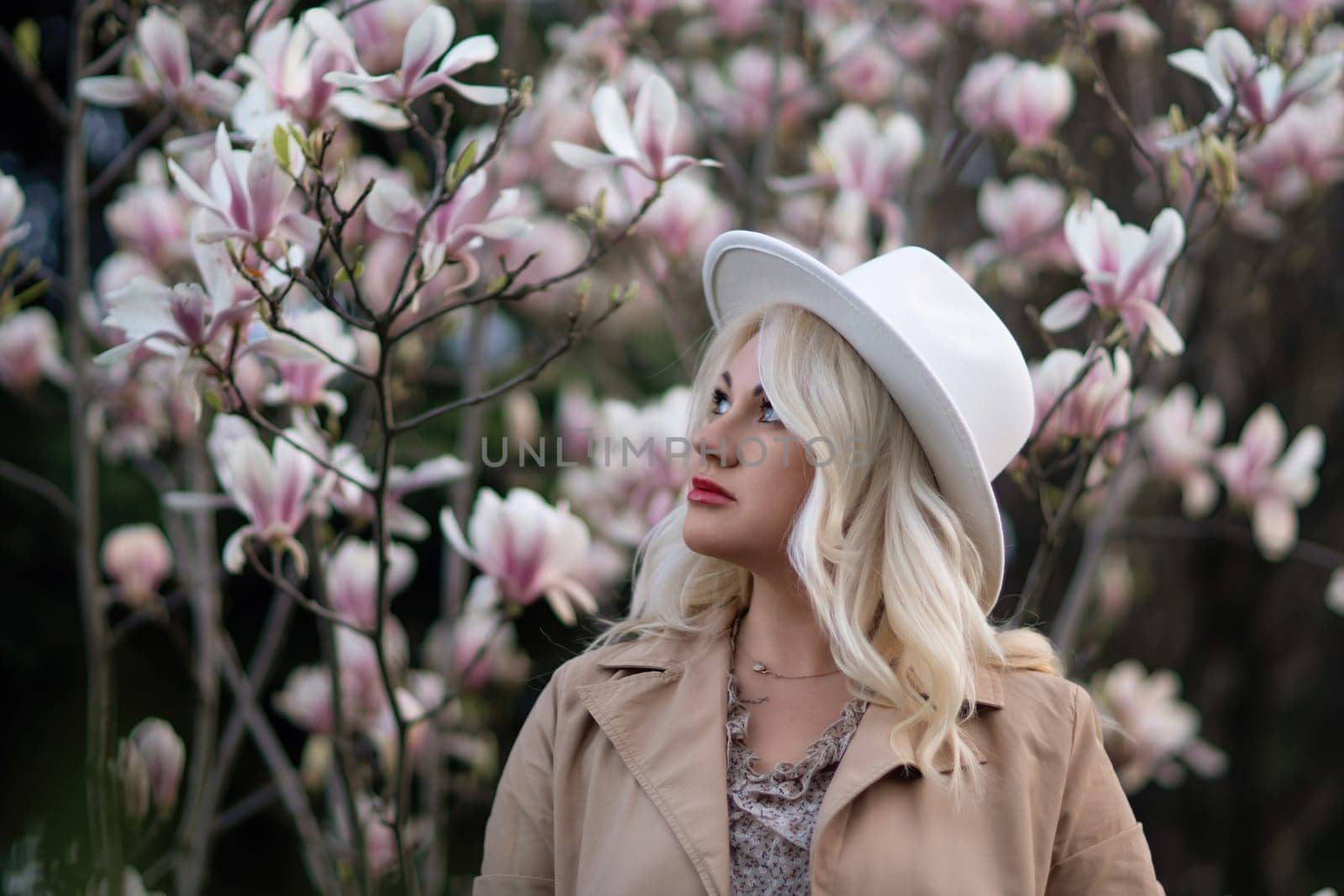 Magnolia flowers woman. A blonde woman wearing a white hat stands in front of a tree with pink flowers