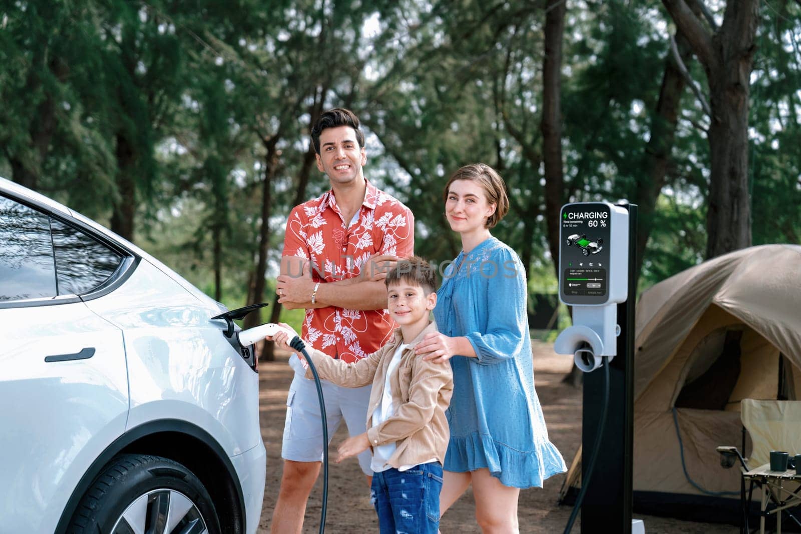 Outdoor adventure and family vacation camping in nature travel by eco friendly car for sustainable future. Lovely family recharge EV car with EV charging station in campsite. Perpetual