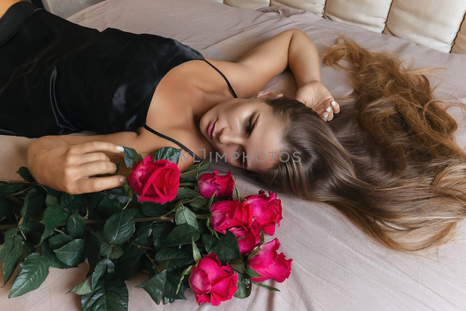 A woman is laying on a bed with a bouquet of red roses next to her. Concept of romance and intimacy, as the woman is surrounded by the flowers and he is in a relaxed and comfortable position. by Matiunina