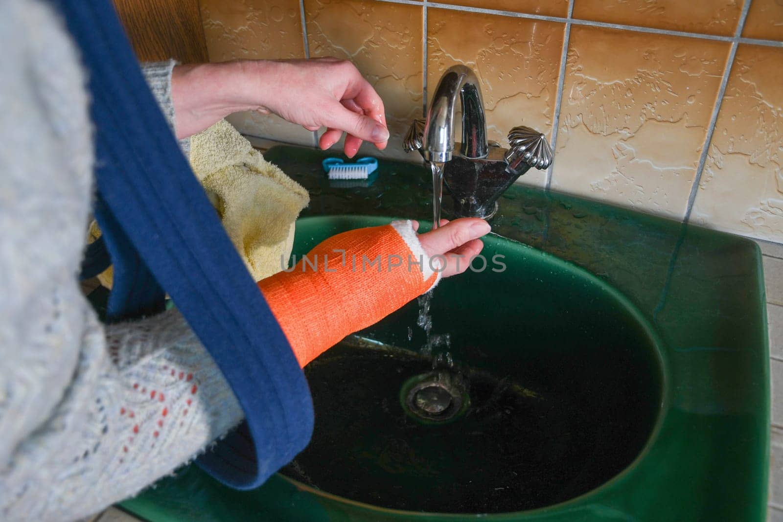 woman with broken arm in cast checks the temperature of the tap water for washing her hands, the concept of changes in the sensitivity of the limb after an injury, high quality photo