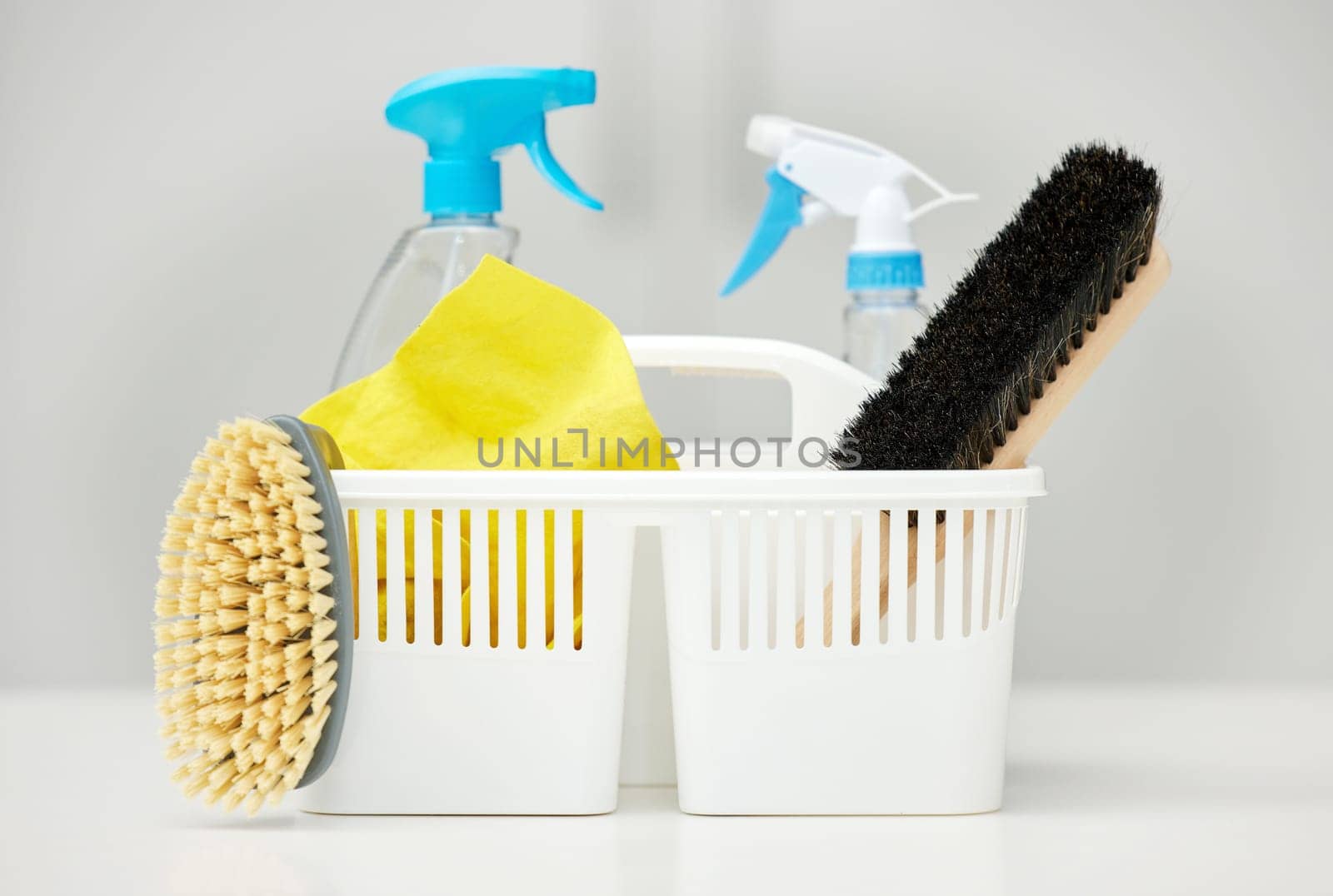 Table, brush or basket with supplies, spray bottle or chemical for bacteria, wellness or dirty mess in home. Grey background, cleaning service or ready for washing with product, liquid soap or gloves.