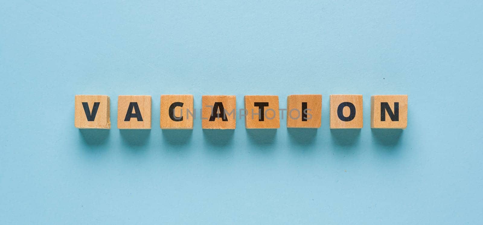 Vacation is written on wooden cubes on a blue background by Sonat