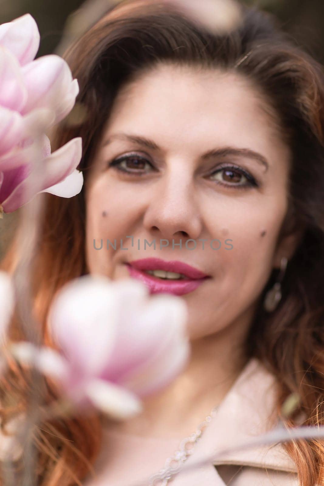 Woman magnolia flowers, surrounded by blossoming trees, hair down, wearing a light coat. Captured during spring, showcasing natural beauty and seasonal change