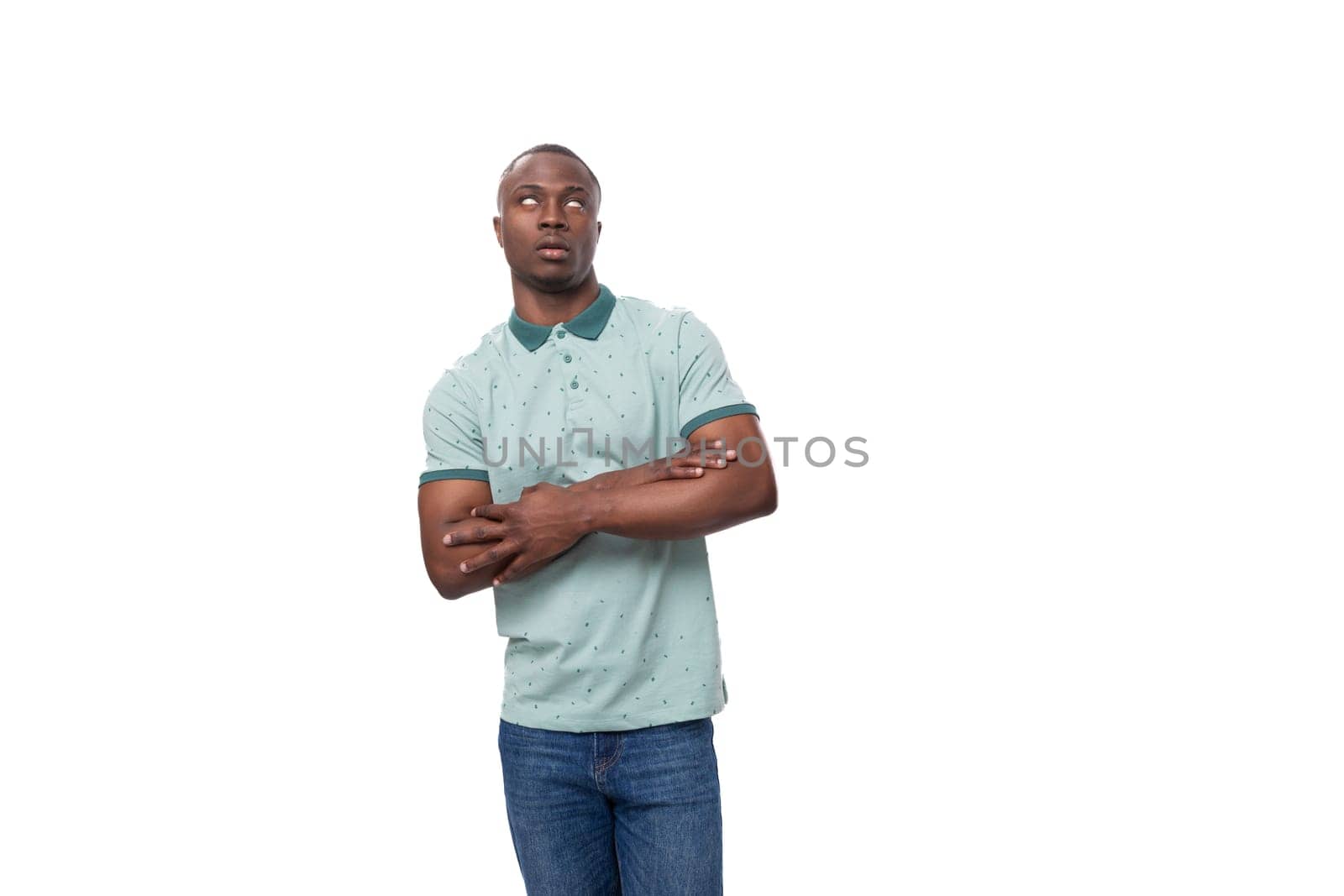 a young slender American man dressed in a T-shirt and jeans stands thoughtfully on a white background.