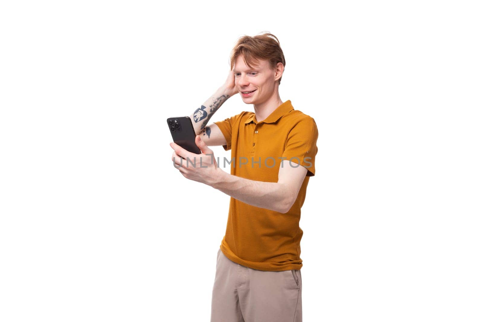 a young guy with short red hair dressed in a summer T-shirt uses social networks in a smartphone by TRMK
