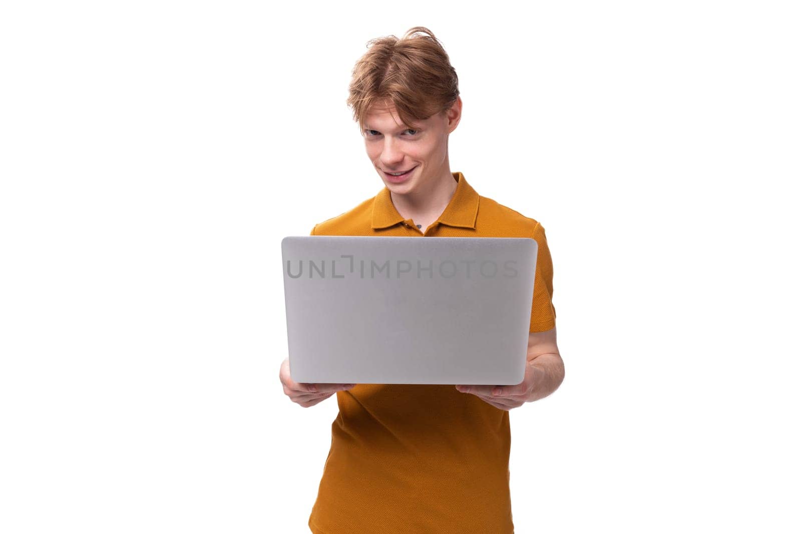 successful IT specialist young red-haired caucasian male student with a tattoo dressed in a mustard t-shirt with a laptop in his hands by TRMK