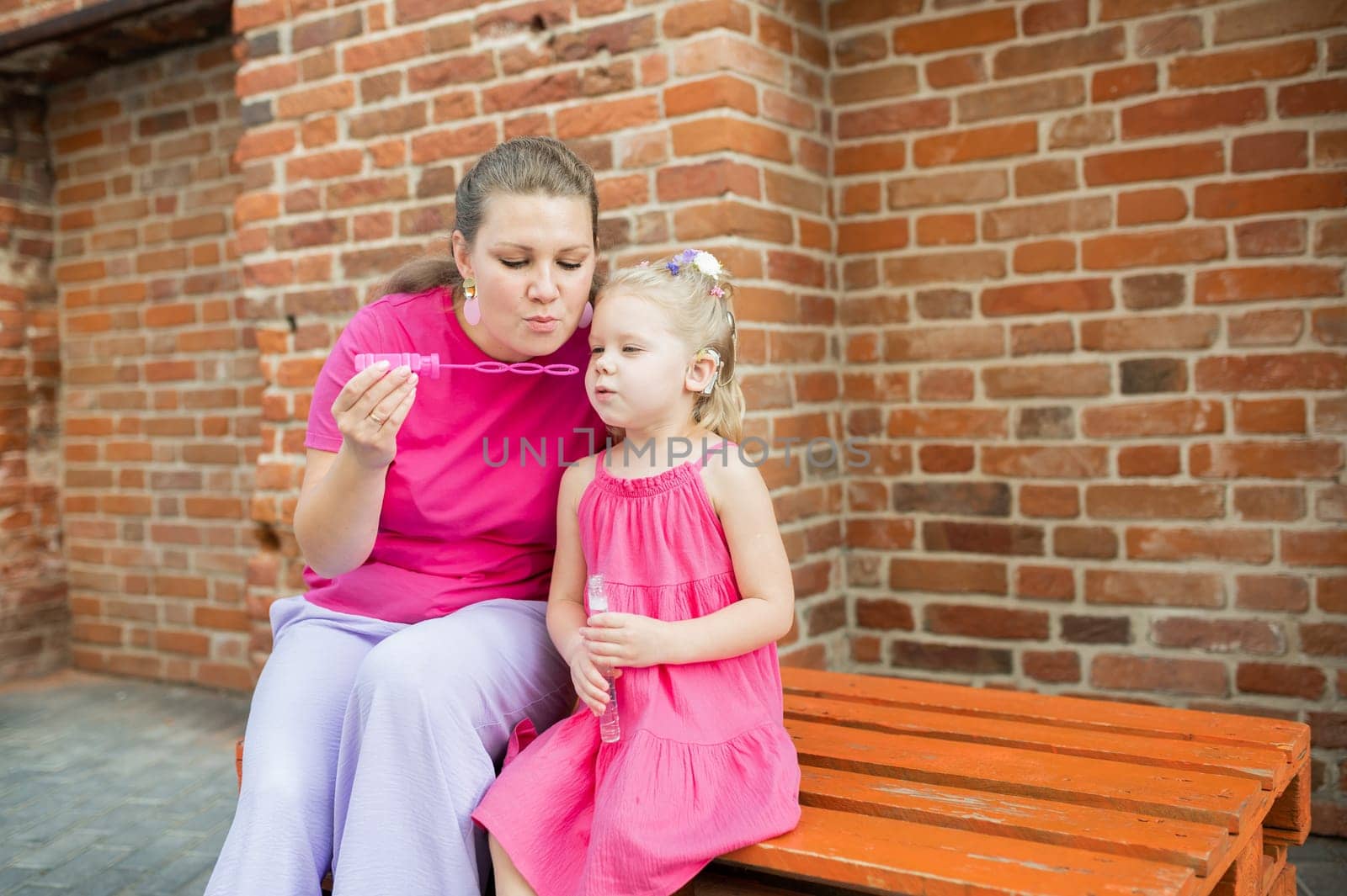 Deaf child with cochlear implant for hearing audio and aid for impairment having fun and laughs with mother outdoor in summer. Sound fitting device to help with communication listening and interaction.