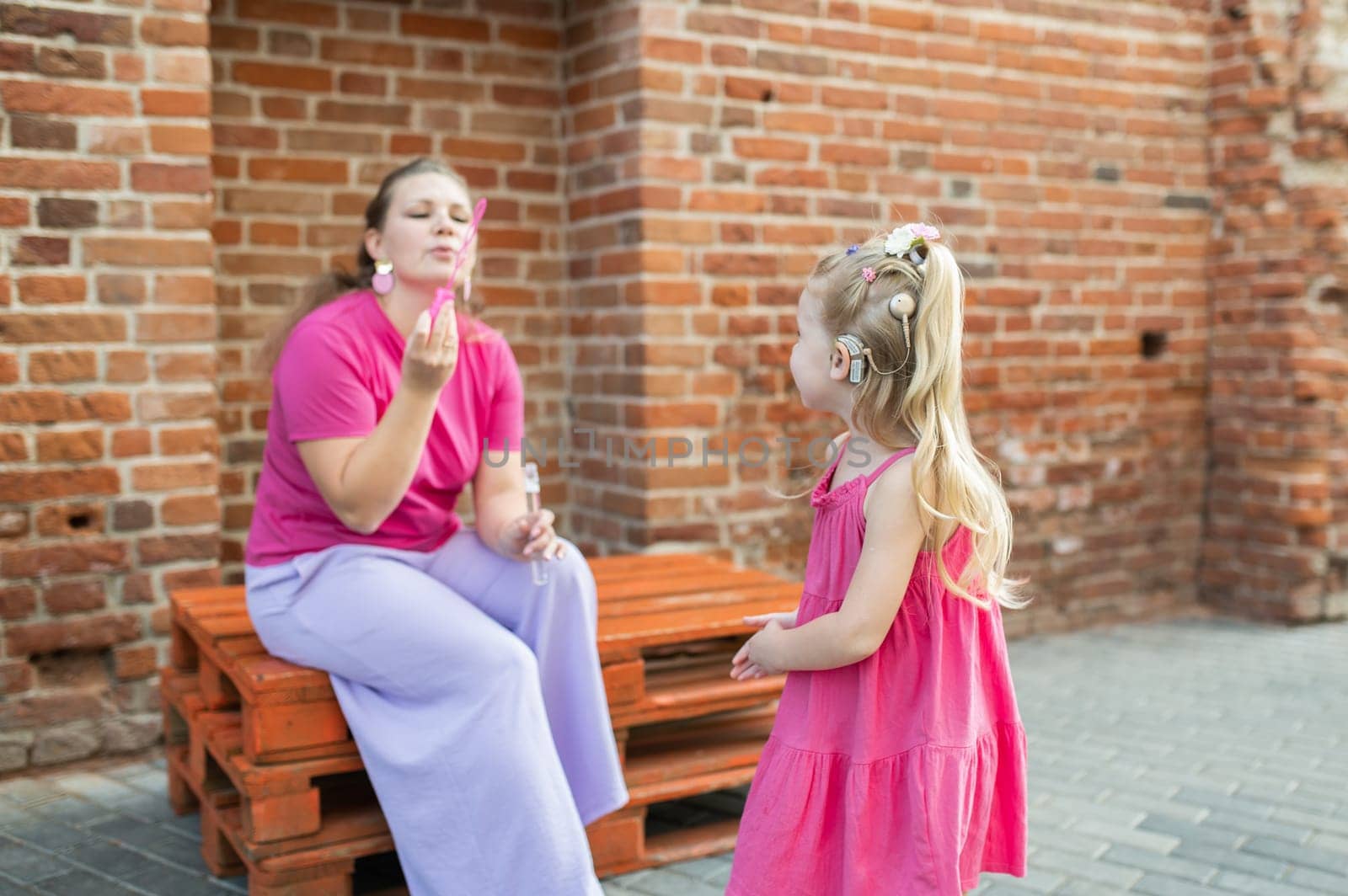 Deaf child with cochlear implant for hearing audio and aid for impairment having fun and laughs with mother outdoor in summer. Sound fitting device to help with communication listening and interaction.