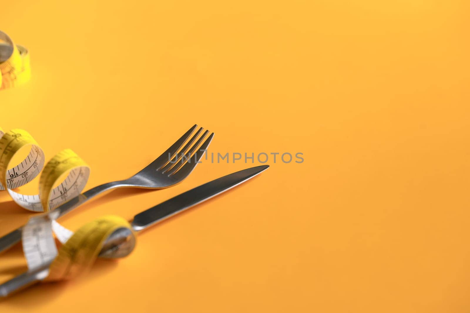 Measuring tape around fork and knife on yellow background. Weight loss and healthy concept.