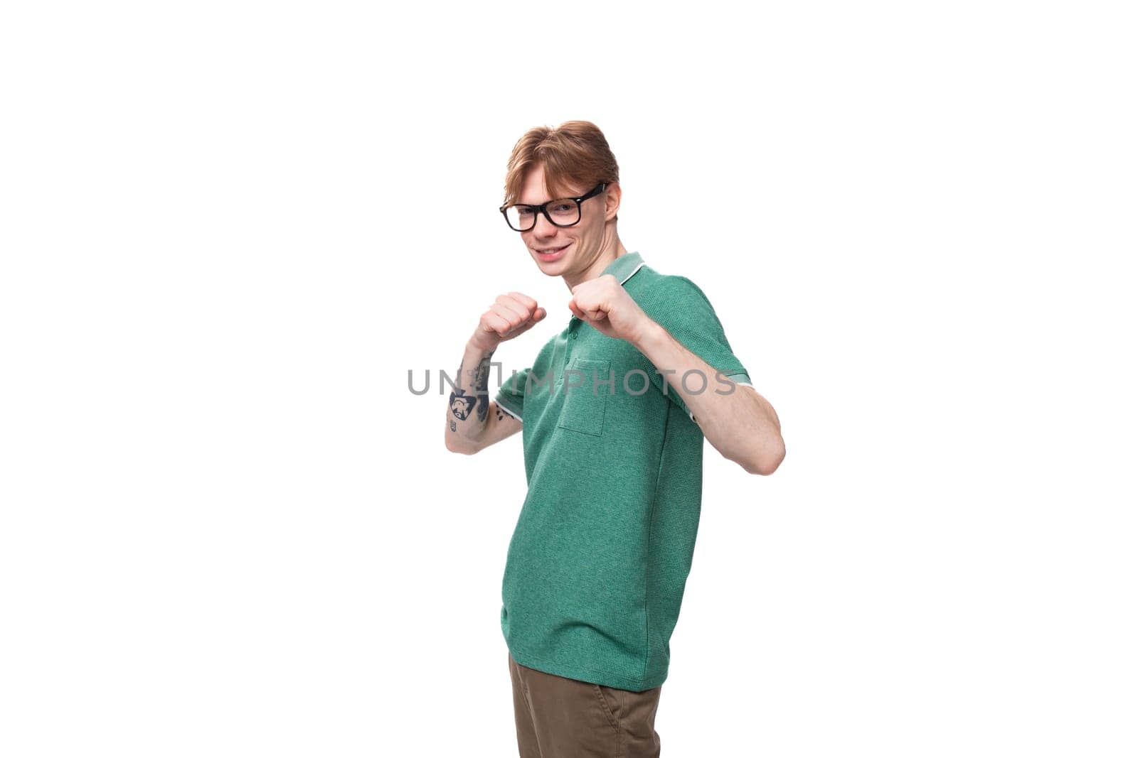 young bright ginger man with a tattoo on his arm dressed in a green short sleeve t-shirt posing on a white background.
