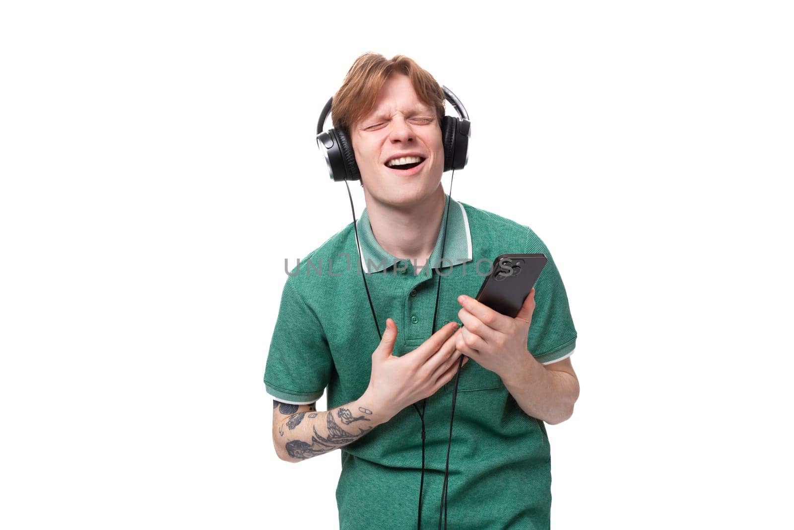 modern stylish energetic young red-haired guy in a green t-shirt listens to music in headphones by TRMK